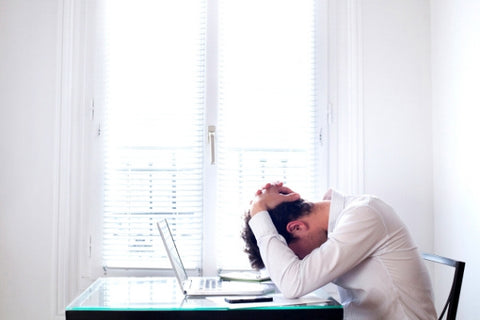 Managing stress in healthy ways. Man sitting at table with head in hands. 