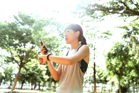 Woman checking cell phone and watch in running clothes outdoors.