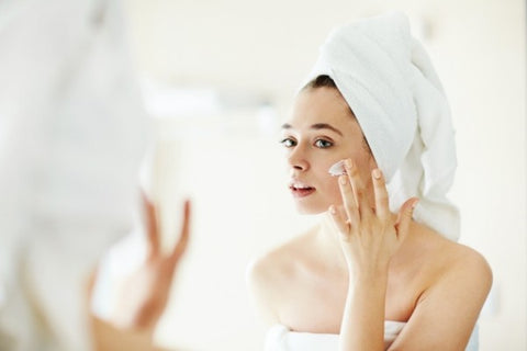 Woman with white towel on applying face cream. 