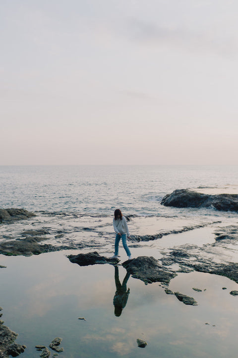 person-stands-on-rocks-poking-out-of-the-ocean-shoreline